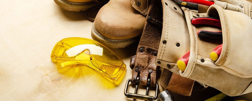 Construction concept background of toolbelt yellow boots goggles ant tools on plywood